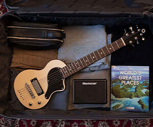 weiße Blackstar Carry-On Reisegitarre verpackt im offenen Koffer mit gefalteter Kleidung und Mini-Verstärker